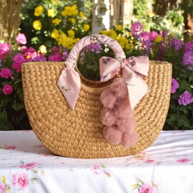 Dara Straw Pom Pom Bag with pink bows and pastel pom poms, handmade in Thailand for weddings and beach days