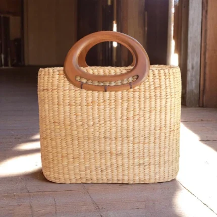 Handmade straw bag with oval wooden handles and square body.