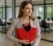 Woman in an office holding a red half-moon straw bag