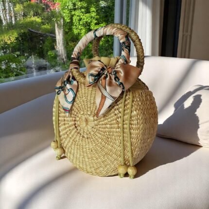Tall oval straw tote with zip top, round scarf-wrapped handles, and decorative drawstring beads