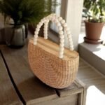 Tassanee Oval Straw Bag With White Bead Handles On Wooden Table