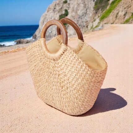 Natural straw tote bag with wooden handles on a beach