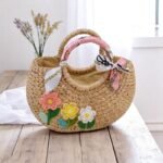Handmade water hyacinth straw bag with floral crochet embroidery, scarf-wrapped handles, and rounded silhouette